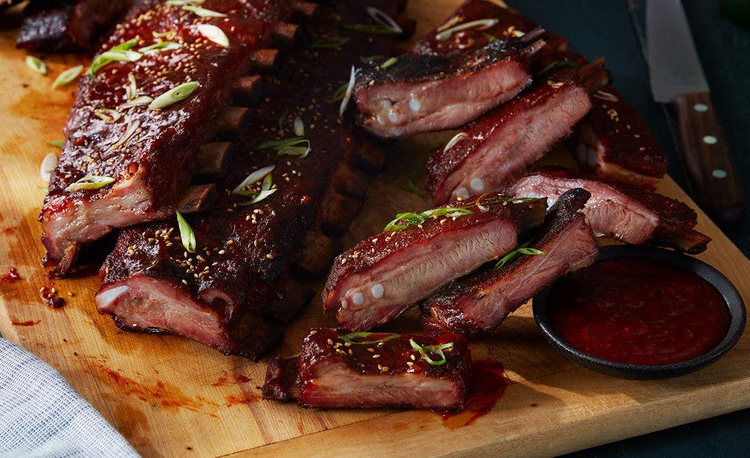 Stack of barbecued pork ribs piled high on a cutting board with a side of sauce