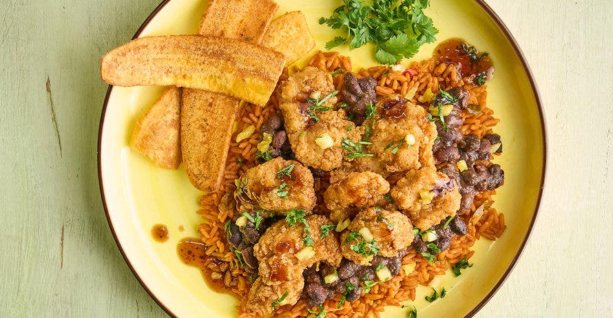 A plate of fried chicken over rice and beans with fried plantains and cilantro