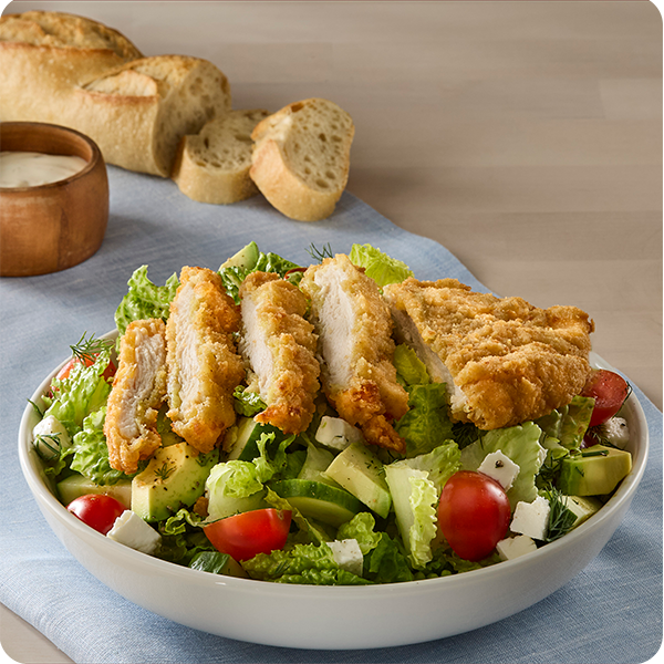 Sliced crispy chicken breast over a chopped salad with tomatoes, avocado, and feta.