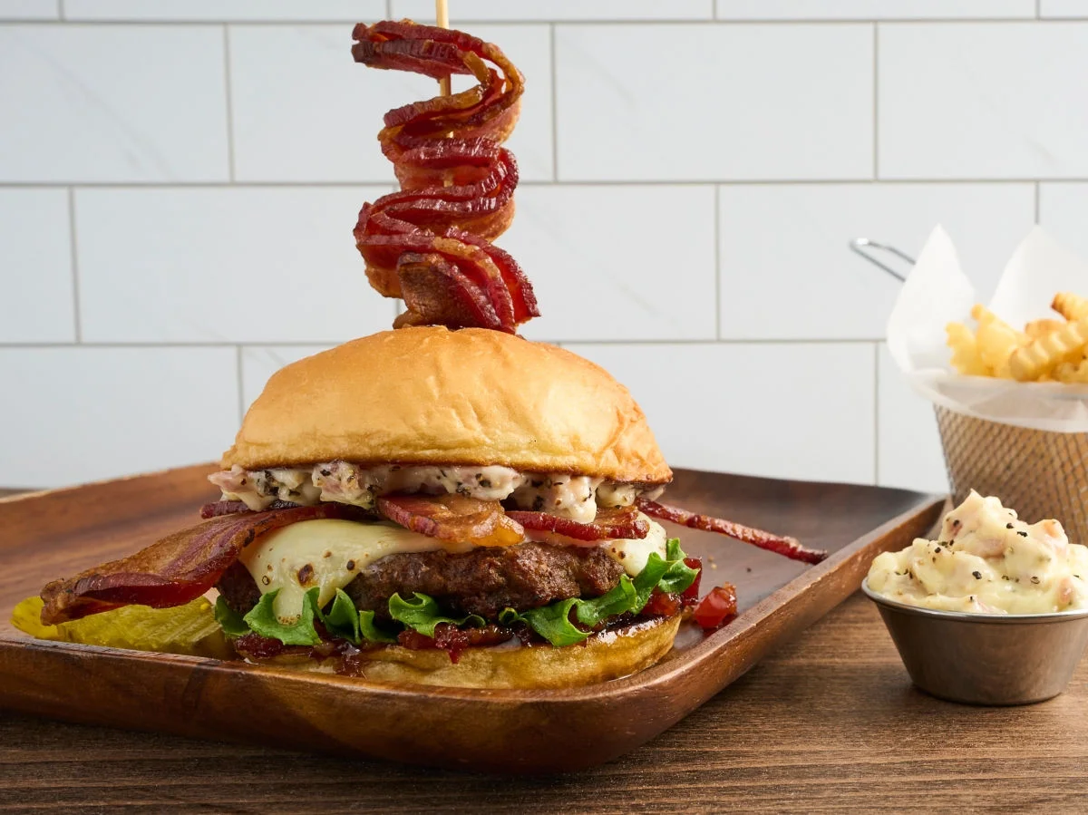 Burger with bacon cheese and lettuce on a wood plate with a side of fries