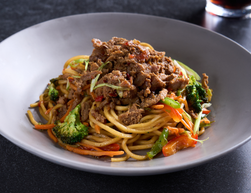 Plated noodles topped with beef, bell peppers and broccoli florets