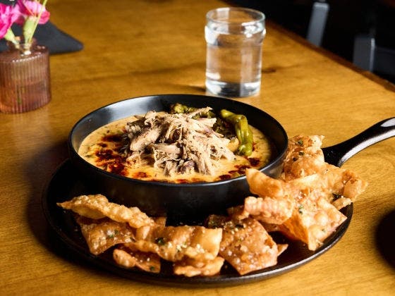 A skillet of creamy dip topped with pulled pork, served with crispy wonton chips