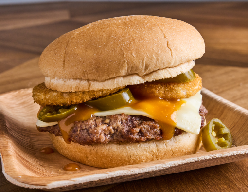 Grilled beef burger with smoky barbecue sauce, melted American cheese, jalapeños and onion rings on a white wheat bun 