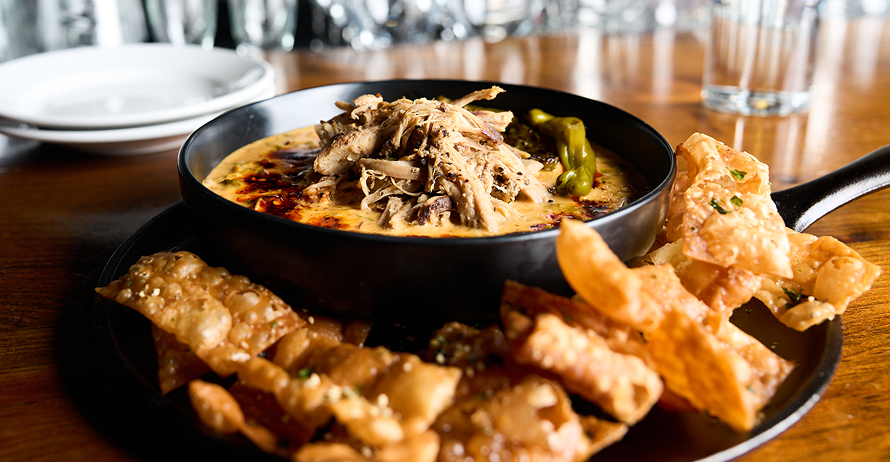 A skillet of creamy dip topped with pulled pork, served with crispy wonton chips