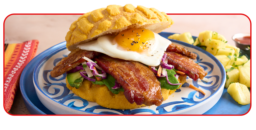 bacon egg breakfast sandwich on a blue plate with a side of potatoes