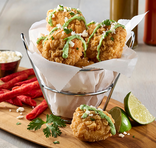 Spicy boneless chicken wings in a basket, topped with cheese and cilantro, served with lime wedges