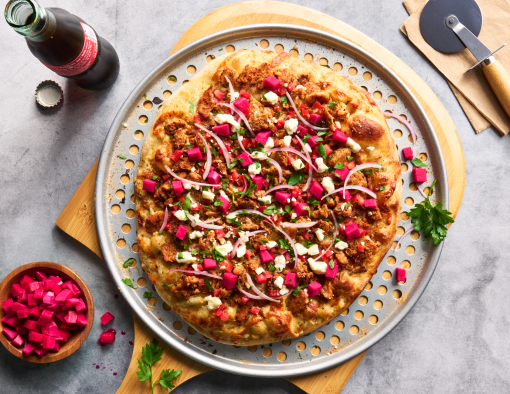 Chicken Shawarma Pizza on a cutting board with a drink and pizza cutter beside it
