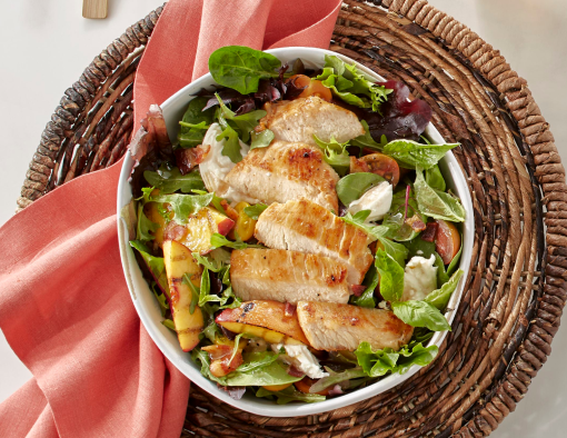 Chicken Breast Filet and grilled peach wedges are placed on a bed of a fresh arugula and spring mix