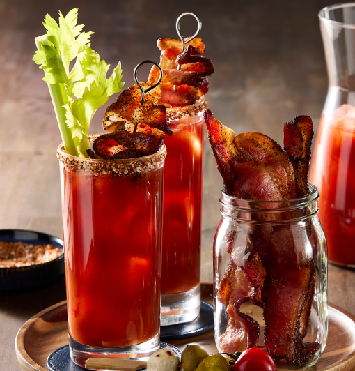 Two Bloody Marys with spiced rims, garnished with celery and crispy bacon