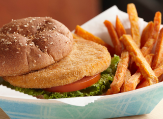 Crispy chicken patty on oat-topped bun with lettuce and tomato, served with sweet potato fries
