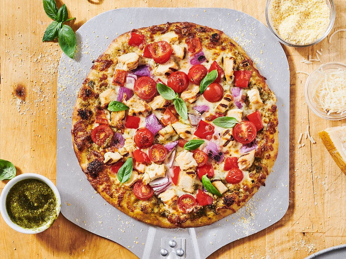 Pesto Chicken Pizza with mozzarella, tomatoes, red onions, bell peppers, and grilled chicken on a peel