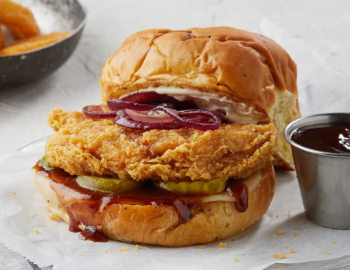 BBQ Chicken Sandwich with a side of onion rings and BBQ sauce on parchment paper