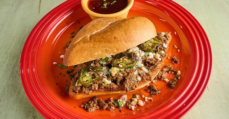 Birra cheesesteak with meat, cheese, and jalapeños on a red plate with a side of dipping sauce