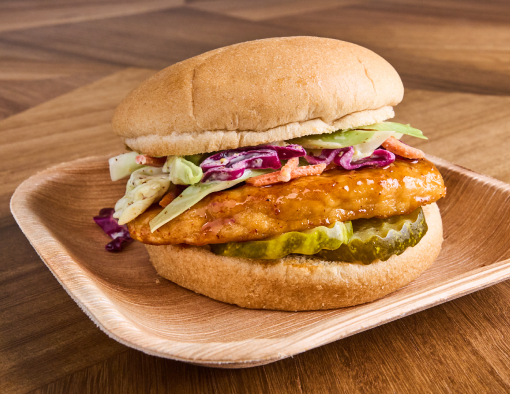 A plate with a grilled chicken patty on a whole-grain bun with sauce and dill pickles 