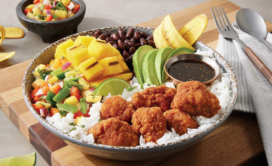 bowl filled with breaded chicken chunks, grilled mango, sliced avocado, plantains and black beans on a bed of rice