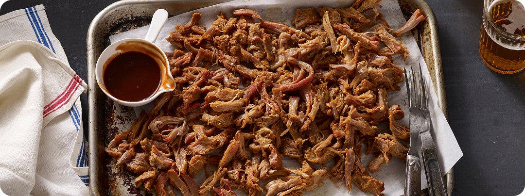 Pulled pork with a side of BBQ sauce on a metal tray