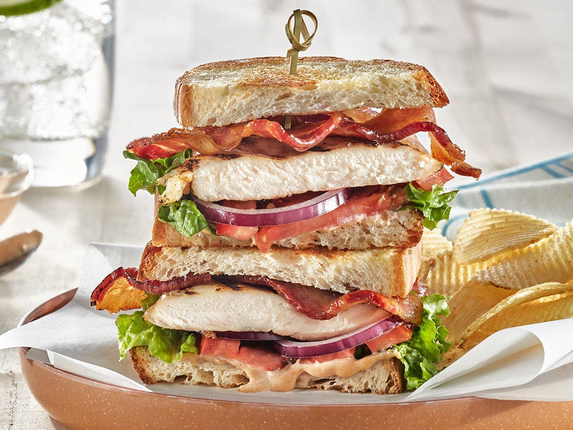 Sandwich with grilled chicken breast, crispy bacon, lettuce, tomato, and red onion on toasted sourdough bread