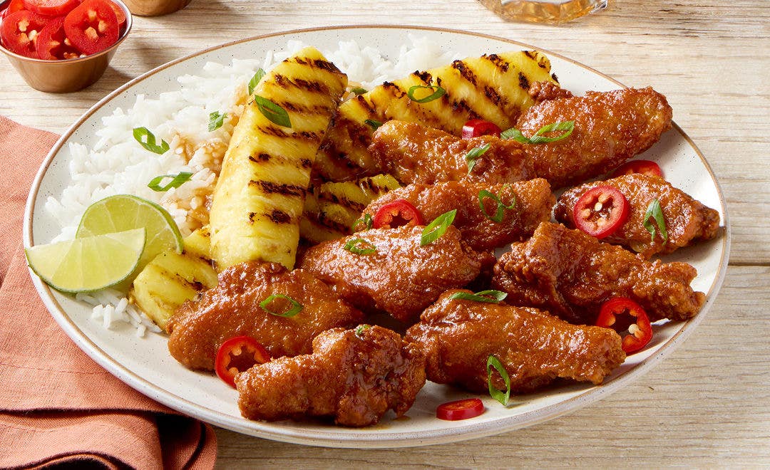 bone-in chicken wings and grilled pineapples on a bed of white rice with lime wedges as garnish