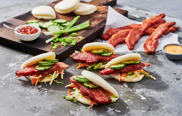 Crispy bacon bao buns with mini cucumbers, hoisin sauce, wasabi mayo, black sesame seeds, and Asian slaw