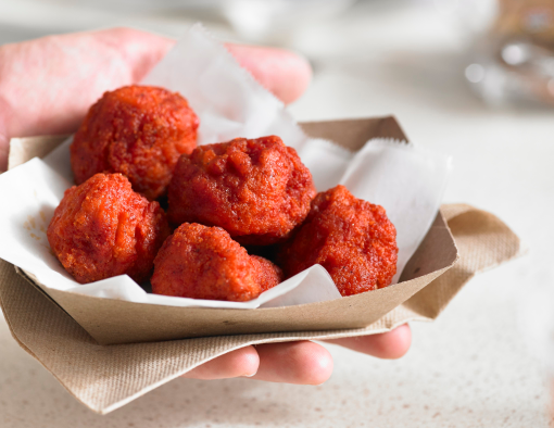 A person’s hand holding small to-go tray of breaded boneless wings 