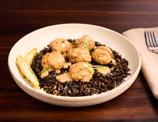 Cajun beef bites with Creole gravy on wild rice, garnished with pickled okra and parsley in a white bowl