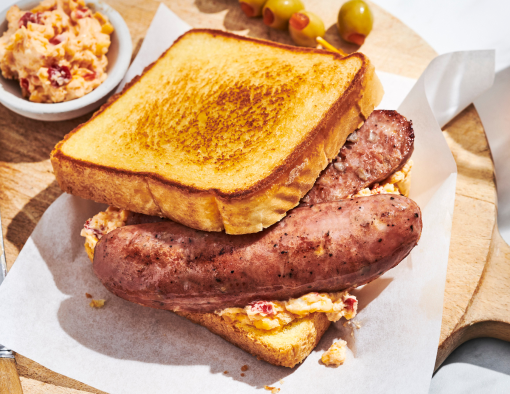 Grilled sausage sandwich with pimento cheese on Texas toast, served on a wooden board