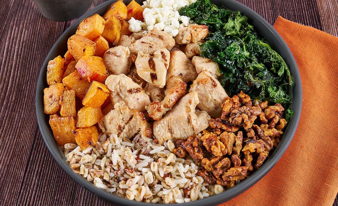 A bowl filled with rice, farro, squash, kale walnuts, goat cheese and chicken chunks  