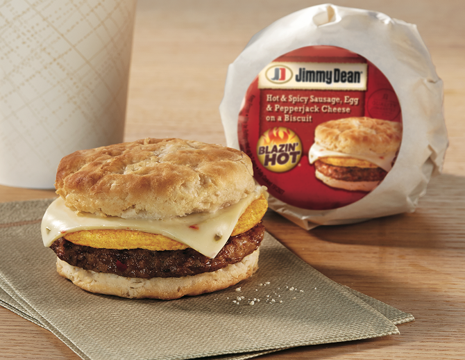 One spicy sausage, egg and cheese sandwich standing upright in a wrapper with a second sandwich unwrapped setting on parchment  