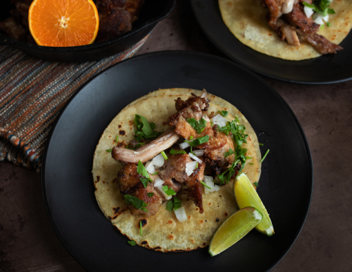 Sous vide pork carnitas on a tortilla with onions, cilantro and lime on a black plate