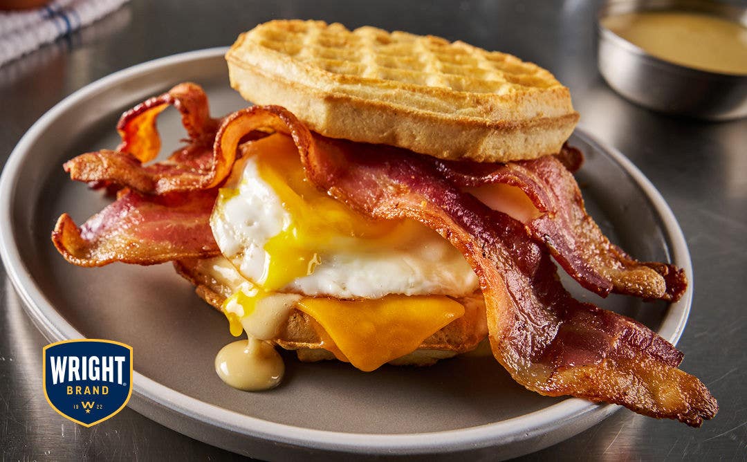 A plate with an egg, cheese, bacon and sauce served sandwiched between two waffles 