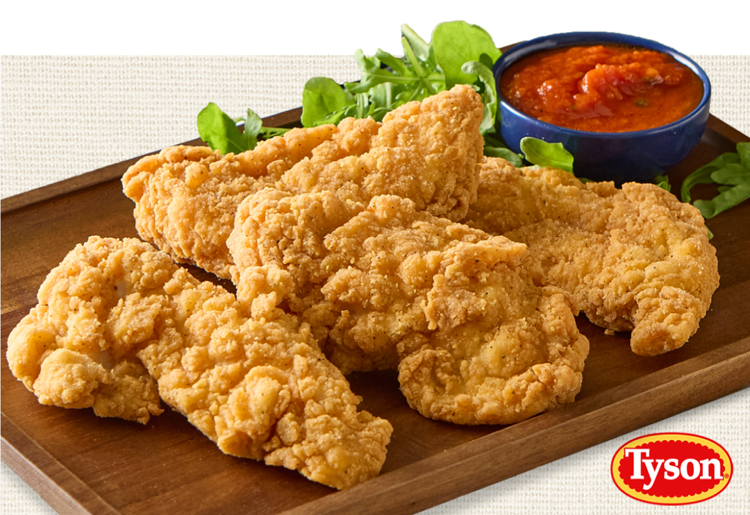 Crispy breaded chicken tenders arranged on a wooden board with a cup of red dipping sauce, leafy greens, and a visible Tyson logo