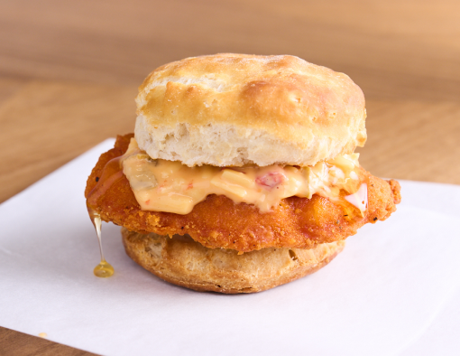 A breaded chicken filet topped with pimento cheese and honey drizzles sandwiched in a biscuit 