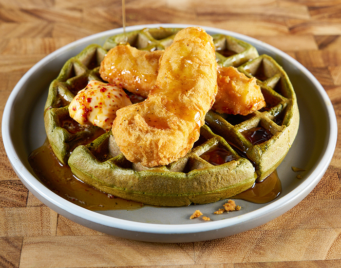 A gray plate with waffle topped with crispy chicken, butter and maple syrup 