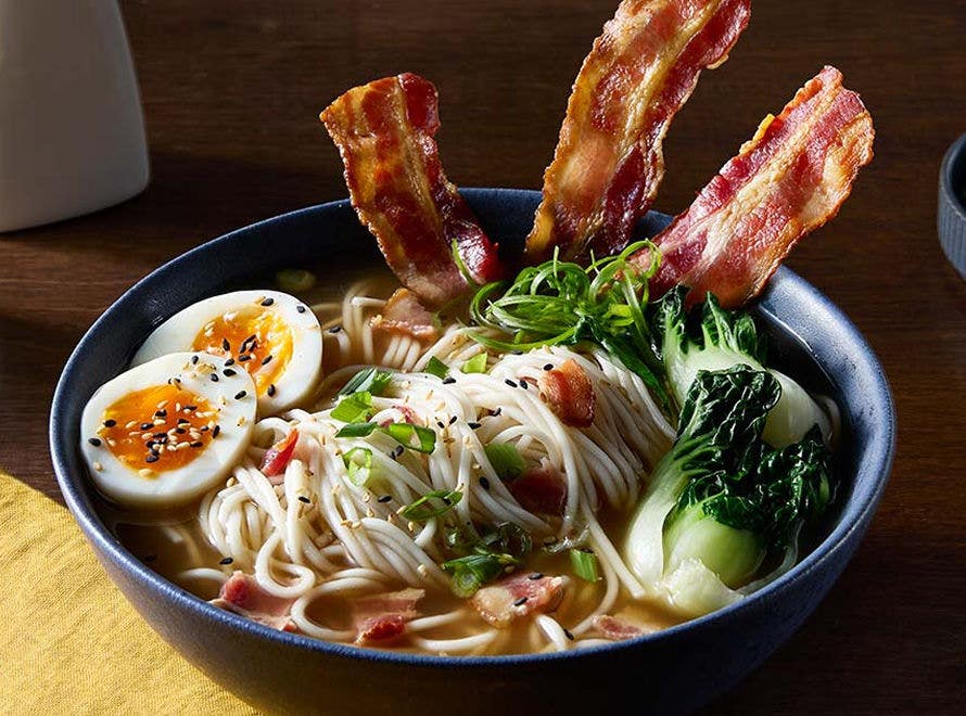 Ramen noodles, bacon, soft-boiled eggs and baby bok choy in a bowl of clear broth 