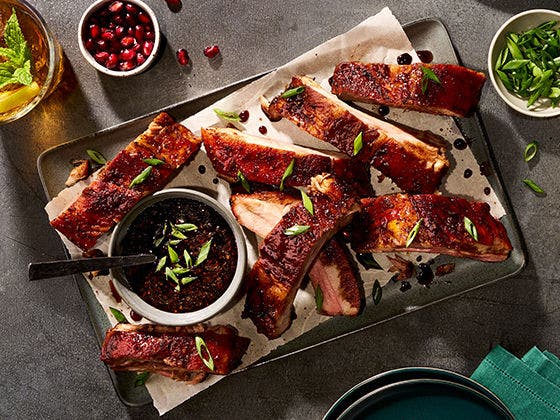 Individual pork baby back ribs in sweet pomegranate molasses glaze, topped with pomegranate seeds and scallions
