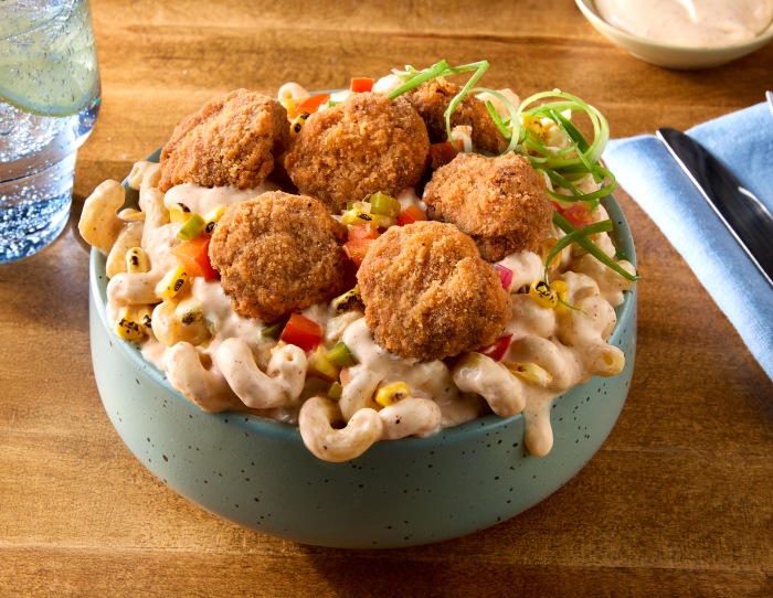 Bowl of creamy macaroni and cheese topped with crispy breaded beef bites, diced peppers, corn, green onions, and a creamy drizzle