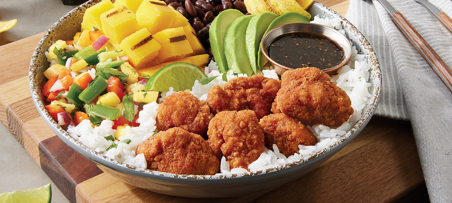 Bowl of crispy fried chicken chunks over white rice with mango, avocado slices, black beans, pico de gallo, and dipping sauce