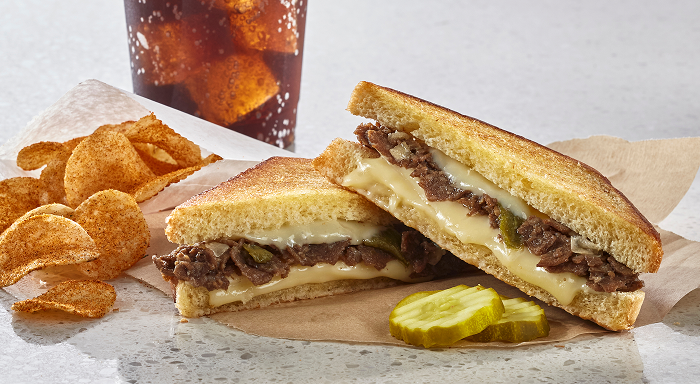 Delicious grilled cheesesteak sandwich served with crispy chips and pickles