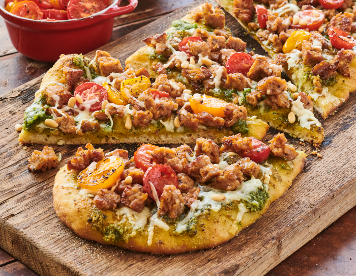 A flatbread loaded with sausage, cherry tomatoes, and cheese served on a cutting board