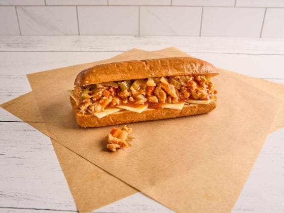 A hoagie roll with sliced chicken, melted provolone, and Chicago-style giardiniera on brown paper