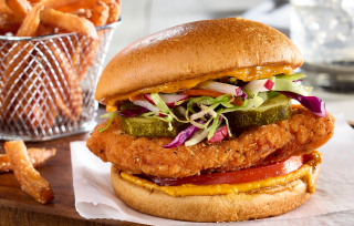 A crispy chicken sandwich with coleslaw, pickles, and tomato, served next to sweet potato fries