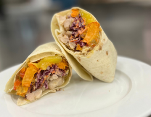 Diced chicken, mango chutney sauce, roasted sweet potatoes and coleslaw in halved tortilla on a plate 