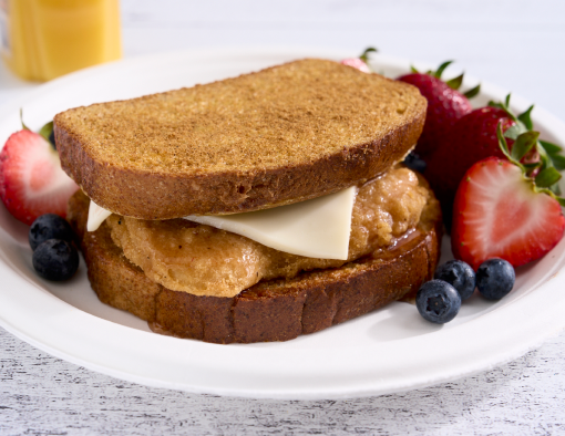 A paper plate with chicken breast filet and cheese slice served on slices of French toast with side of berries 
