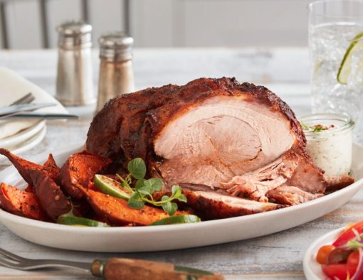 Roasted pork butt sliced with vegetables and garnish served on a white plate placed on a table