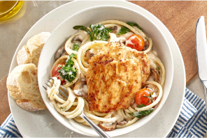 Chicken breast on top of noodle soup and vegetables with a side of bread 