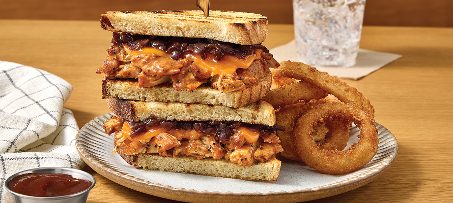 Stacked smoked pulled chicken sandwich on toasted bread with melted cheese and barbecue sauce, served with crispy onion rings on a plate with drink