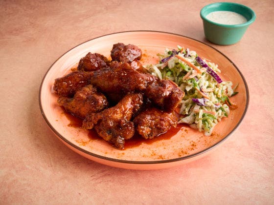 Saucy chicken wings and coleslaw on a peach plate with a small bowl of creamy dipping sauce