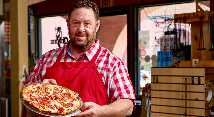 Man is red aperon holding a pizza