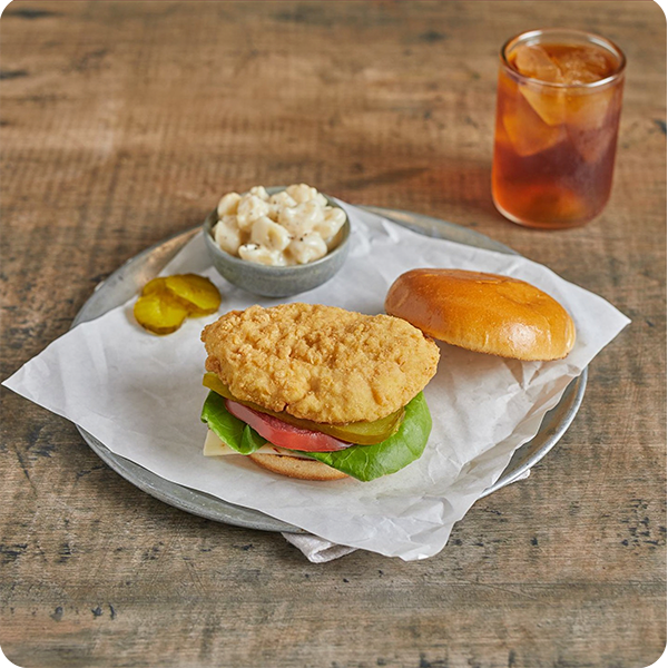 Crispy chicken breast sandwich with lettuce, tomato, and pickles, served with macaroni salad.