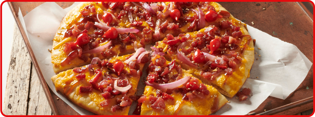 A sliced round pizza with a golden crust hosts bacon and pineapple with a side of parmesan cheese.